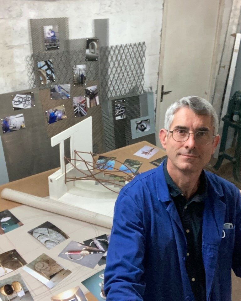 Emmanuel Dhellin, artisan du métal, dans son atelier lors des Jema 2018, avec des photos de ses œuvres et une maquette de passerelle.