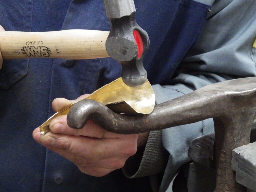Gros plan sur les mains D'Emmanuel Dhellin qui martèle une pièce métallique. Photo prise au cours d'une démonstration faite lors des Jema 2018