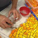Patrick Abat colle des tesselles en smalti.Photo qui permet en 1 clic d'accéder au programme JEMA 2024 de l'atelier de Mosaïque Mosaïc Concept à Antony