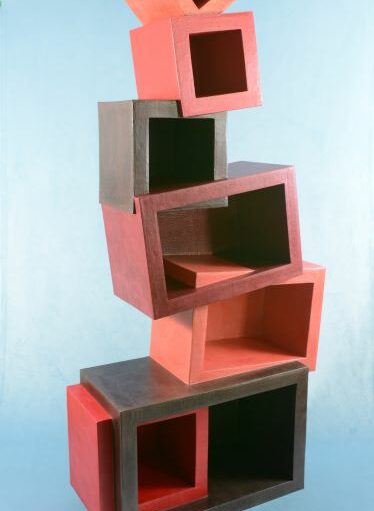 EMA 2024-autour du carton-meuble géométrique : Grand meuble en carton composé de différents cubes et rectangles (tons rouge et brun) empilés les uns sur les autres donnant une impression d'équilibre instable.