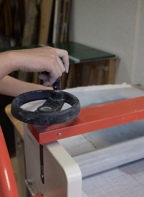 Image centrée sur une main réglant la machine utilisée pour la fabrication des feuilles de carton-pierre.Atelier Louis Jean Rigal